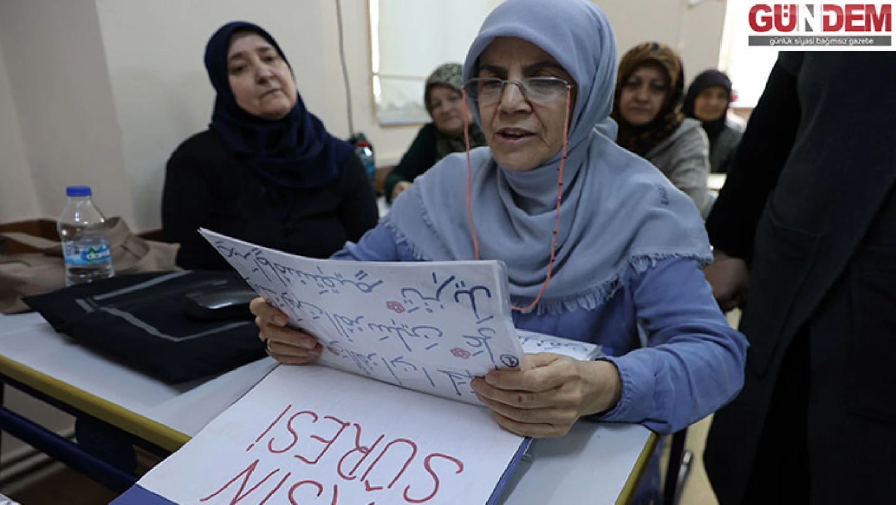Kur'an kursu öğreticisi, az gören kursiyere ayetleri büyük harflerle yazarak destek veriyor